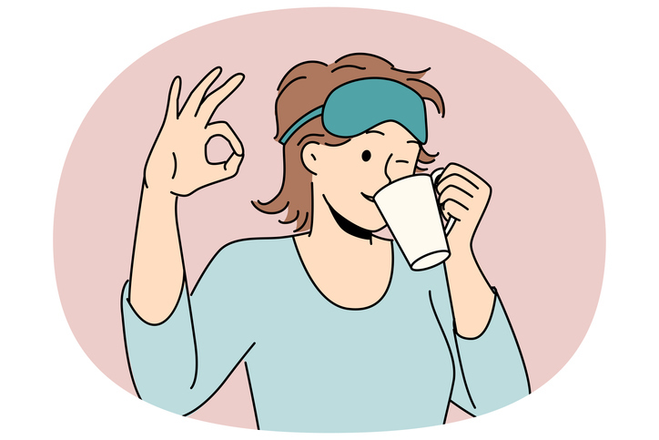 Woman drinks morning coffee after waking up and shows ok gesture standing in sleep mask and pajamas. Girl winks enjoying hot coffee or tea drink to cheer up and get ready for work day