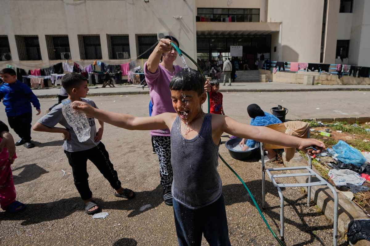 19일 레바논 남부에서 이스라엘의 공습을 피해 시돈으로 대피한 여성이 임시 대피소로 사용 중인 학교 운동장에서 아들에게 물을 뿌려주고 있다. 뉴시스