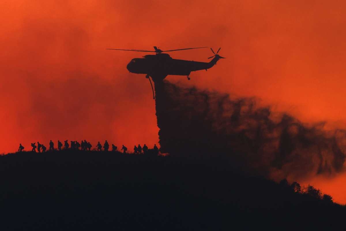 A water tanker drops water while firefighters walk below, as the Sandy Fire approaches, Tuesday, May 19, 2026, in Simi Valley, Calif. (AP Photo/Caroline Brehman)